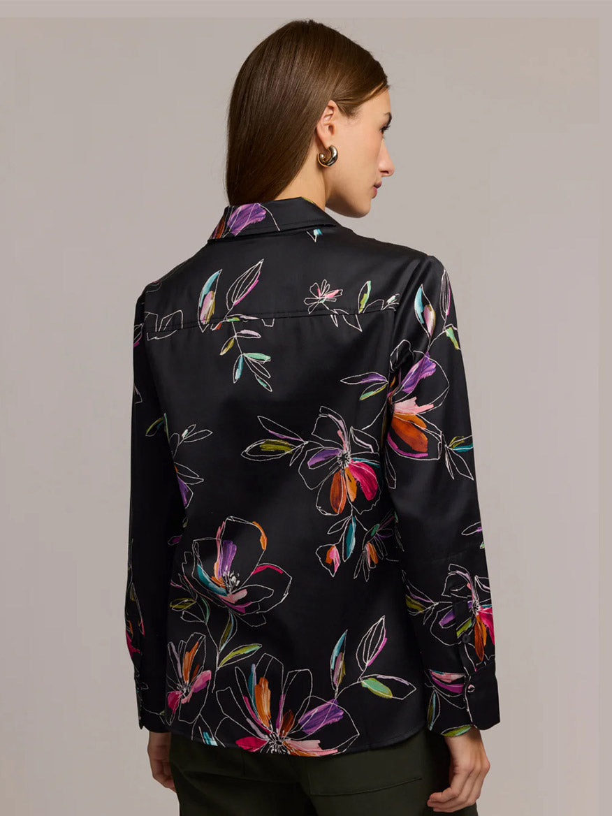 A woman with straight brown hair is shown from the back wearing the Hinson Wu Margot Long Sleeve Floral Stencil Shirt in Black, a relaxed-fit blouse crafted from a cotton-blend satin with a colorful floral print.
