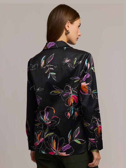 A woman with straight brown hair is shown from the back wearing the Hinson Wu Margot Long Sleeve Floral Stencil Shirt in Black, a relaxed-fit blouse crafted from a cotton-blend satin with a colorful floral print.