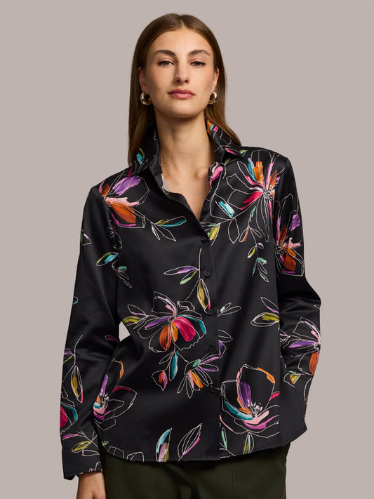 A woman wears the Hinson Wu Margot Long Sleeve Floral Stencil Shirt in Black—a relaxed-fit black button-up crafted from luxurious cotton blend satin with a colorful floral pattern—standing against a plain grey background.