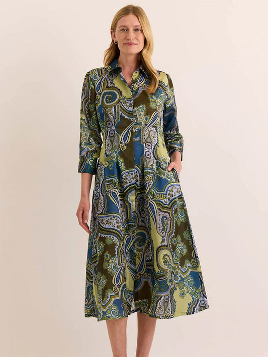 A woman stands against a plain background wearing the Hinson Wu Martina 3/4 Sleeve Opulent Dress in Olive Paisley, a button-down midi dress adorned with an elegant paisley print in shades of green, blue, and brown. Crafted from premium Italian polyester fabric with a fluid drape and silky hand feel, this dress effortlessly combines comfort and sophistication.