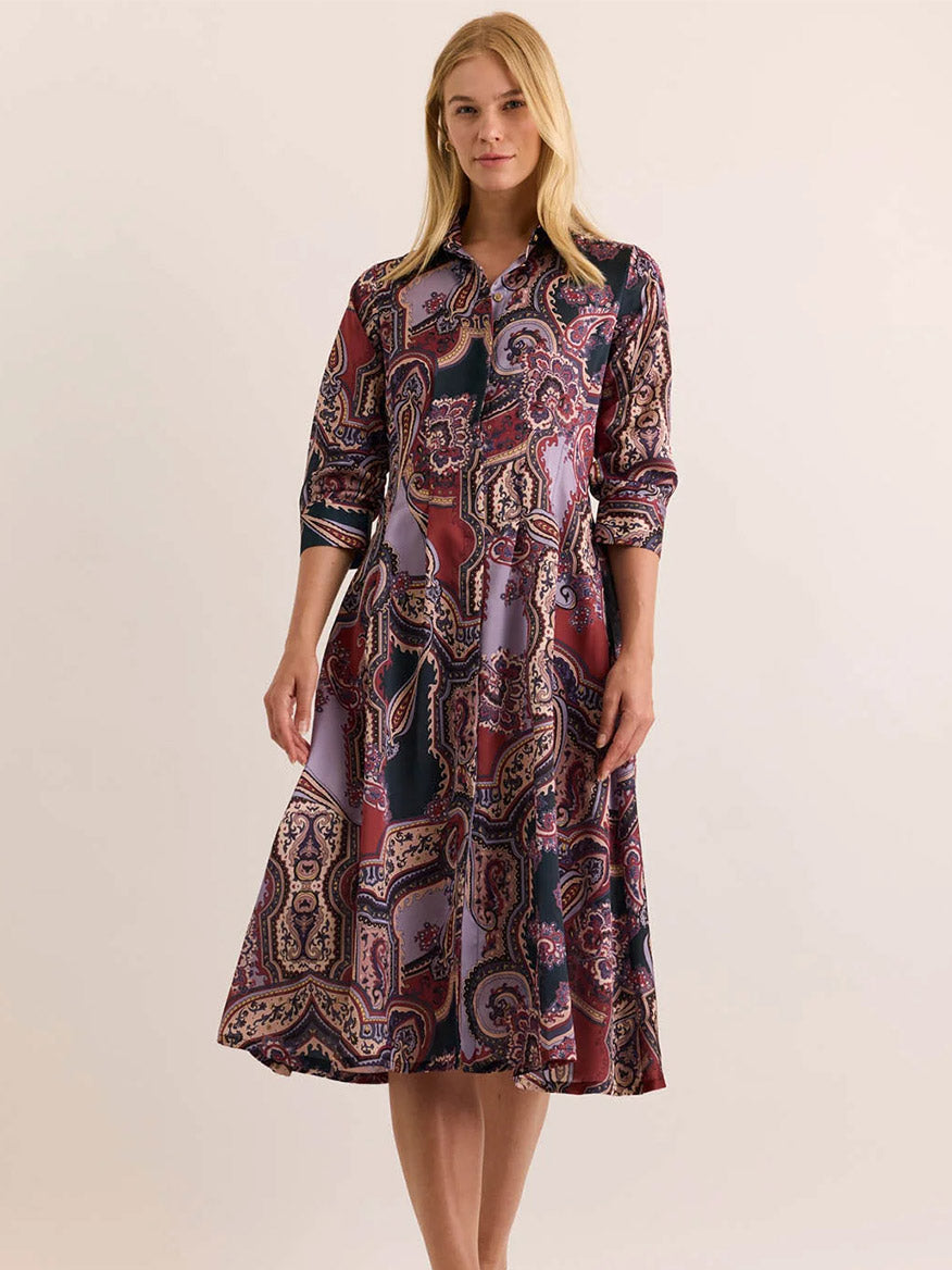 A woman stands against a plain background wearing the Hinson Wu Martina 3/4 Sleeve Opulent Dress in Plum Paisley, a midi-length button-down dress featuring a vibrant paisley pattern in shades of maroon, purple, and green. Crafted from luxurious Italian polyester with a fluid drape and silky hand feel, this dress moves beautifully with every step.