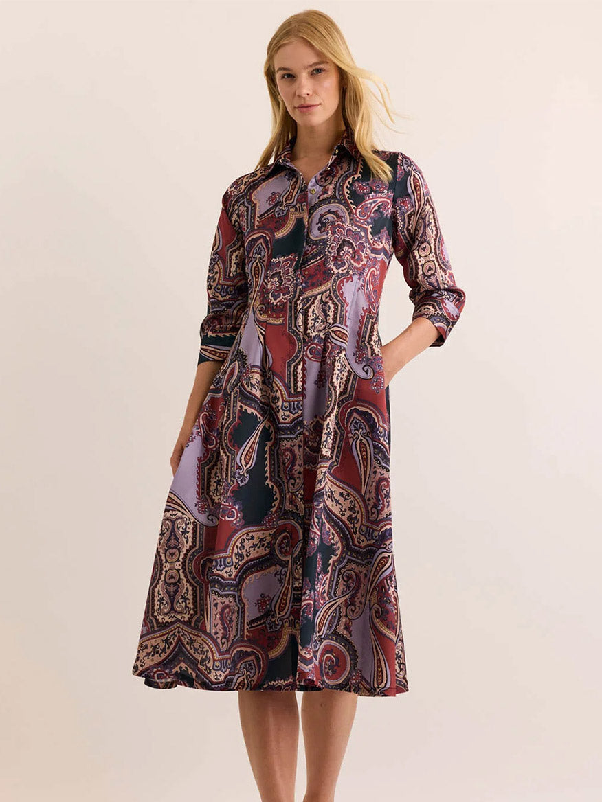 A woman stands against a plain light background, wearing the Hinson Wu Martina 3/4 Sleeve Opulent Dress in Plum Paisley—a midi-length, button-down dress with pockets, featuring an elegant paisley pattern and crafted from Italian polyester fabric for a silky feel and fluid drape.