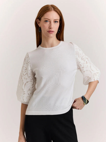 A woman with long auburn hair wears the Hinson Wu Millie Lace Elbow Sleeve Sweater in white and black pants, standing with one hand on her hip against a plain background.