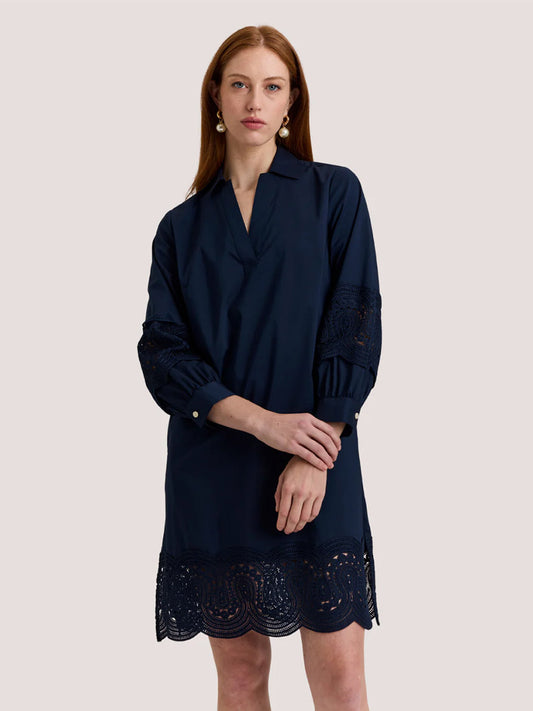 A woman stands against a plain light background wearing the Hinson Wu Mona Bracelet Sleeve Lace Dress in Navy, featuring stretch polished cotton and lace details on the sleeves and hem.