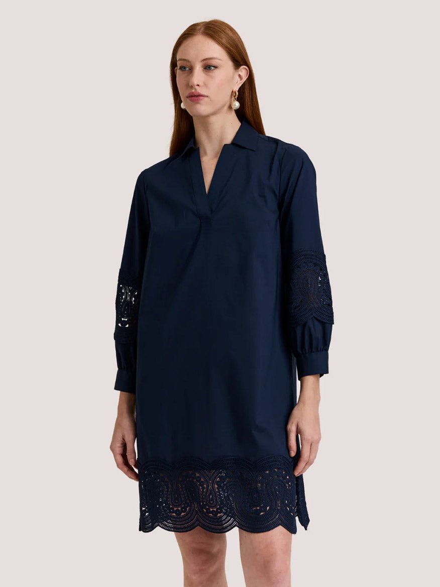 A woman wears the Hinson Wu Mona Bracelet Sleeve Lace Dress in Navy, featuring eyelet lace details on the sleeves and hem, made from stretch polished cotton, standing against a plain light background.