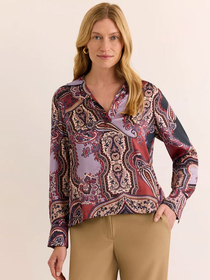 Styled in tan pants, the model showcases the Hinson Wu Mona Long Sleeve Opulent Paisley Top in Plum Paisley—a blouse featuring a sophisticated paisley print in burgundy and lavender hues, meticulously crafted from Italian polyester fabric for a fluid drape and silky hand feel—posed against a plain background.