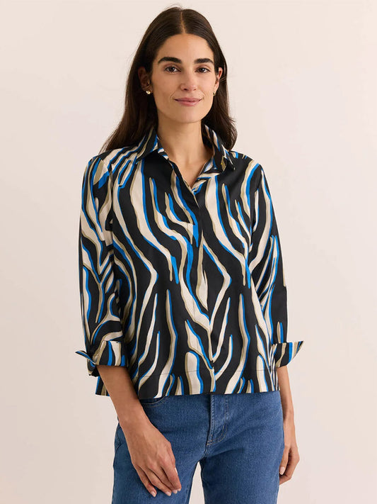 A woman with long brown hair wears the Hinson Wu New Xena 3/4 Sleeve Shirt in Abstract Zebra, featuring a black, white, and blue zebra print crafted from comfortable stretch fabric, paired with blue jeans as she stands against a neutral background.