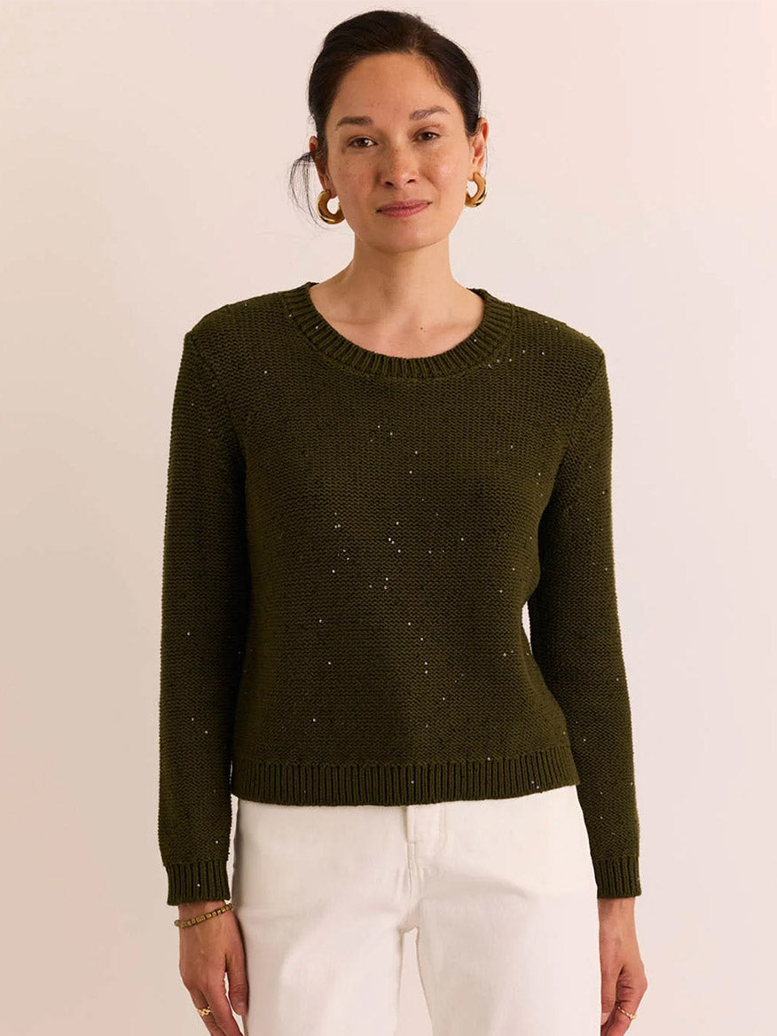 A woman wearing the Hinson Wu Queenie Long Sleeve Sequins Sweater in Oregano pairs it with white pants, standing against a plain light-colored background—perfect for breathable comfort and year-round wear.