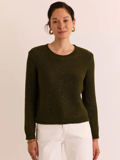 A woman wearing the Hinson Wu Queenie Long Sleeve Sequins Sweater in Oregano pairs it with white pants, standing against a plain light-colored background—perfect for breathable comfort and year-round wear.