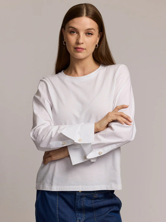 A woman with long brown hair, wearing the Hinson Wu Reagen Long Sleeve Foundation Layer in White and blue jeans, stands with her arms crossed against a plain background.