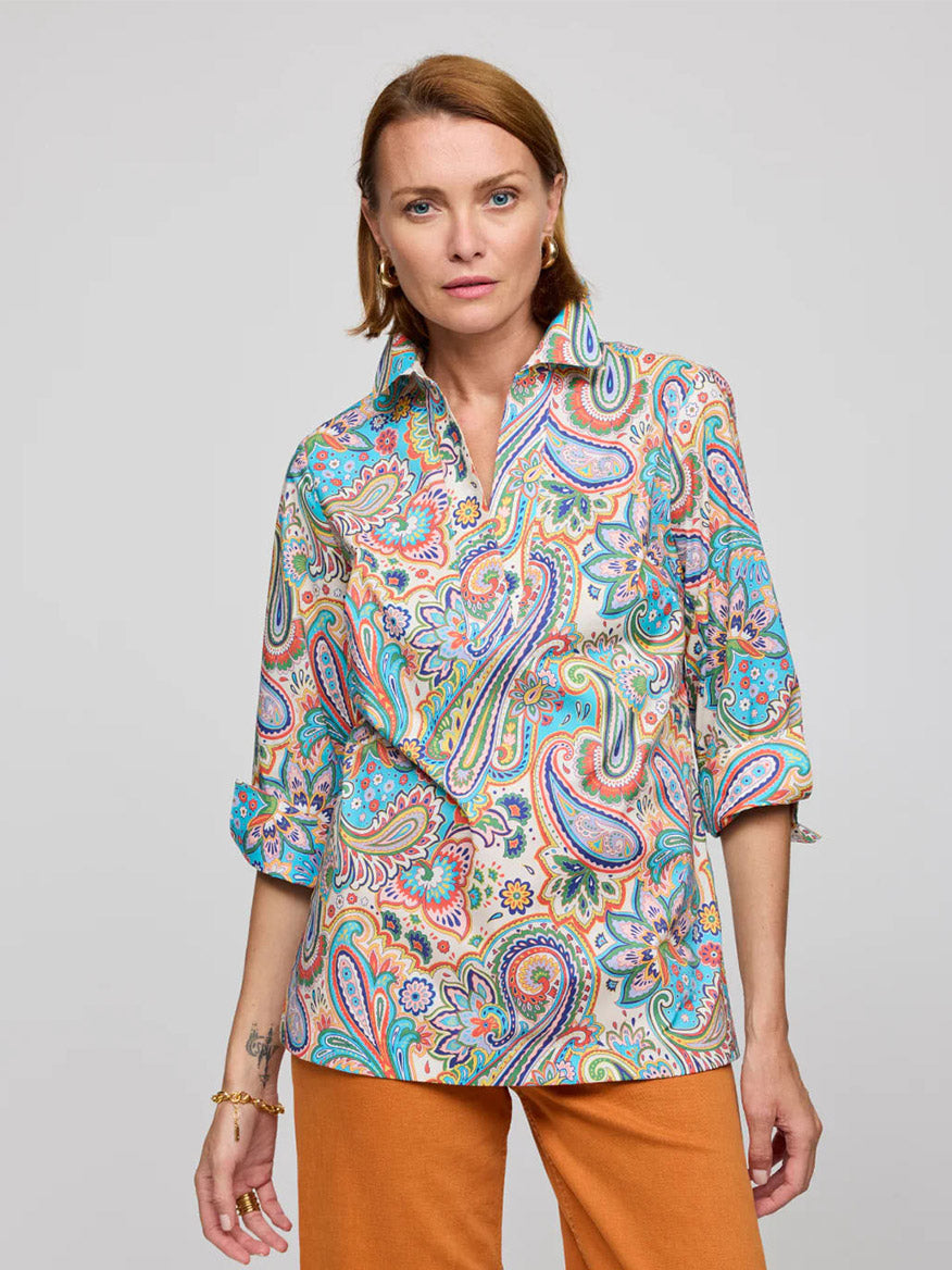 A person dons the Hinson Wu Vicky 3/4 Sleeve Multi Color Paisley Print Top with orange pants against a plain background, highlighting their versatile style.