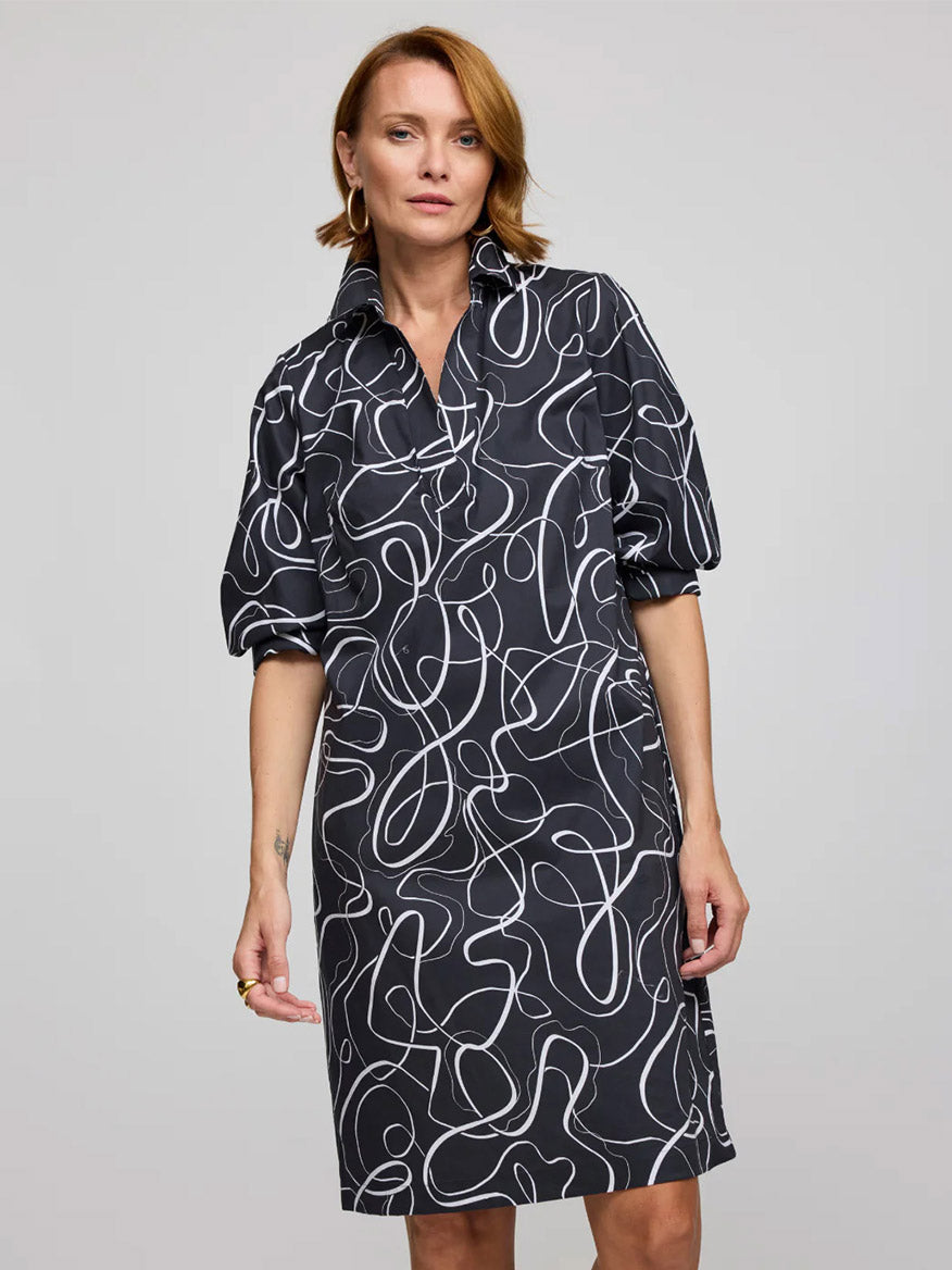 A woman wears the Hinson Wu Vicky 3/4 Sleeve Ribbon Dress in Black/White, featuring a knee-length cut and exclusive white abstract print, standing against a plain gray background.