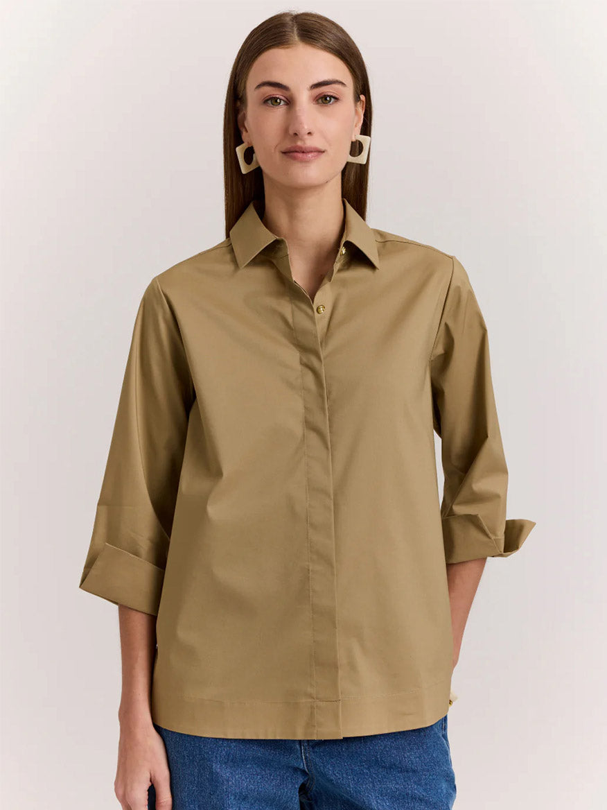 A woman wearing the Hinson Wu Xena 3/4 Sleeve Zip Back Shirt in Khaki and blue jeans stands against a plain light background.