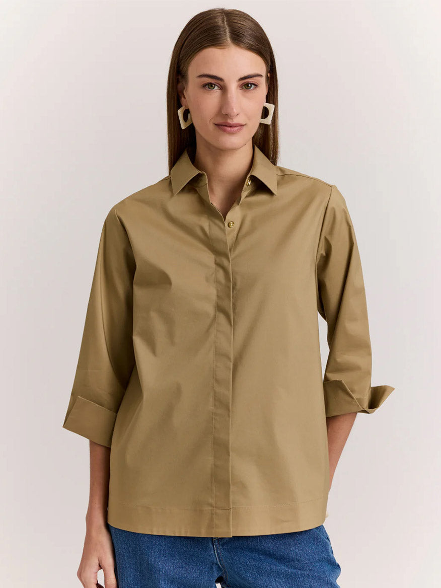 A woman stands against a plain background wearing a khaki Hinson Wu Xena 3/4 Sleeve Zip Back Shirt and blue jeans.
