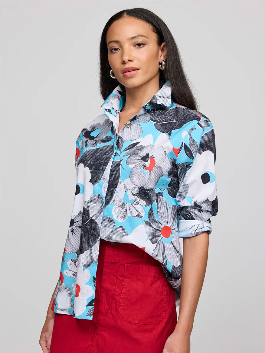 A woman wears the Hinson Wu Xena 3/4 Sleeve Pop Art Flower Shirt in blue, black, white, and red cotton, paired with a red skirt, standing against a plain gray background.