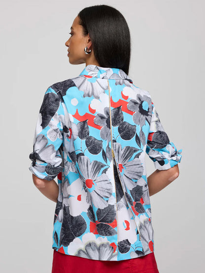 A woman with long dark hair faces away, wearing the Hinson Wu Xena 3/4 Sleeve Pop Art Flower Shirt—a refined cotton piece featuring exclusive bold blue, black, white, and red floral prints; her sleeves are rolled up.