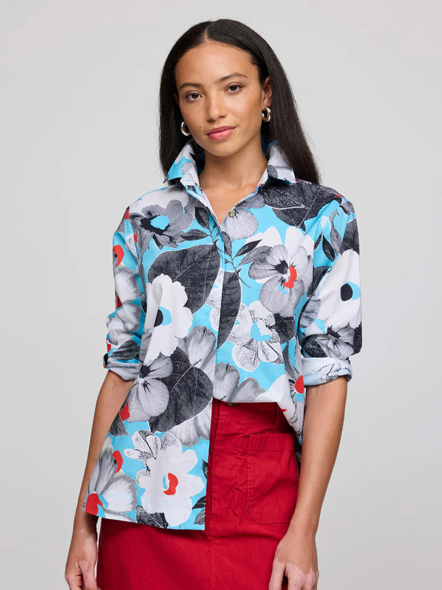A woman with long dark hair wears the Hinson Wu Xena 3/4 Sleeve Pop Art Flower Shirt featuring blue, white, and black floral prints on refined cotton with rolled sleeves, paired with a red skirt against a plain light background.