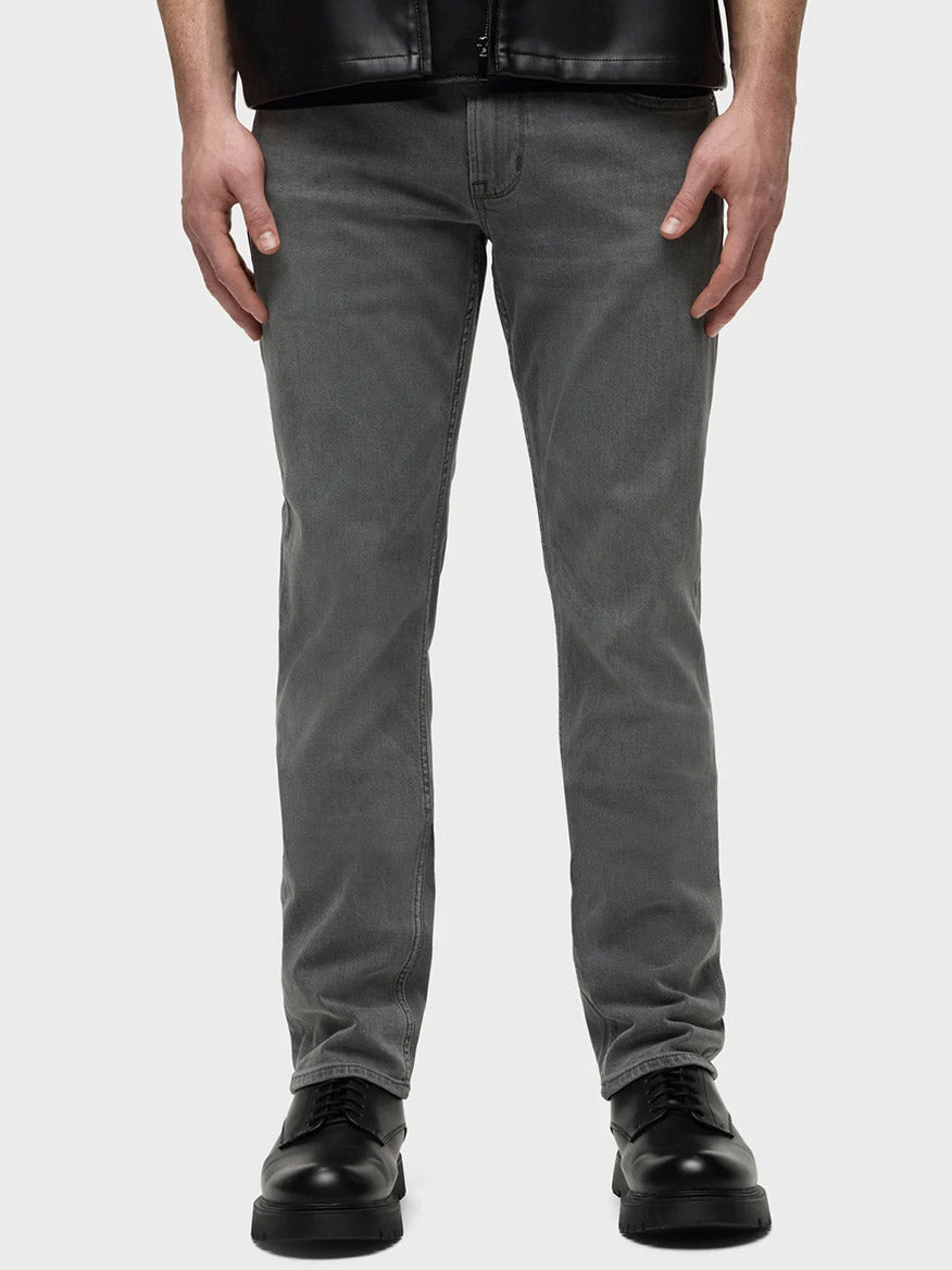 A person in Hudson Blake Slim Straight Jeans in Moon Ridge with a tapered leg and black shoes stands against a plain background, their upper body not visible.