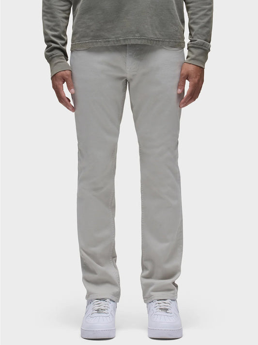 A man stands against a plain white background, wearing dark green long sleeves and white sneakers, complemented by Hudson Blake Slim Straight Twill Pant in Ash with classic five-pocket detailing.