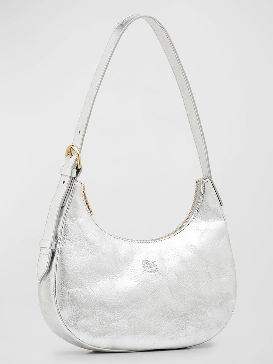 A [Il Bisonte Belcanto Shoulder Bag in Metallic Silver](product link), handmade in Tuscany by Il Bisonte, featuring a silver curved shape, zip closure, gold-tone hardware, and an adjustable strap against a plain background.