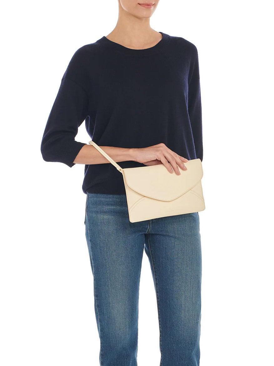 Woman in a navy blue sweater and blue jeans holding an elegant Il Bisonte Esperia Clutch in White Cowhide Leather, with a convenient wrist strap.