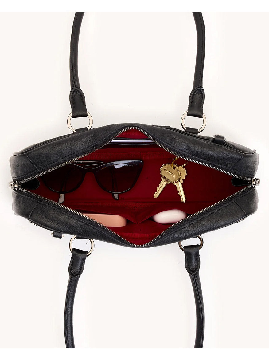 The Hammitt Los Angeles Meredith Small in Black/Gunmetal is shown from above, revealing a red interior that holds sunglasses, a pair of keys, and two pink oval-shaped objects.
