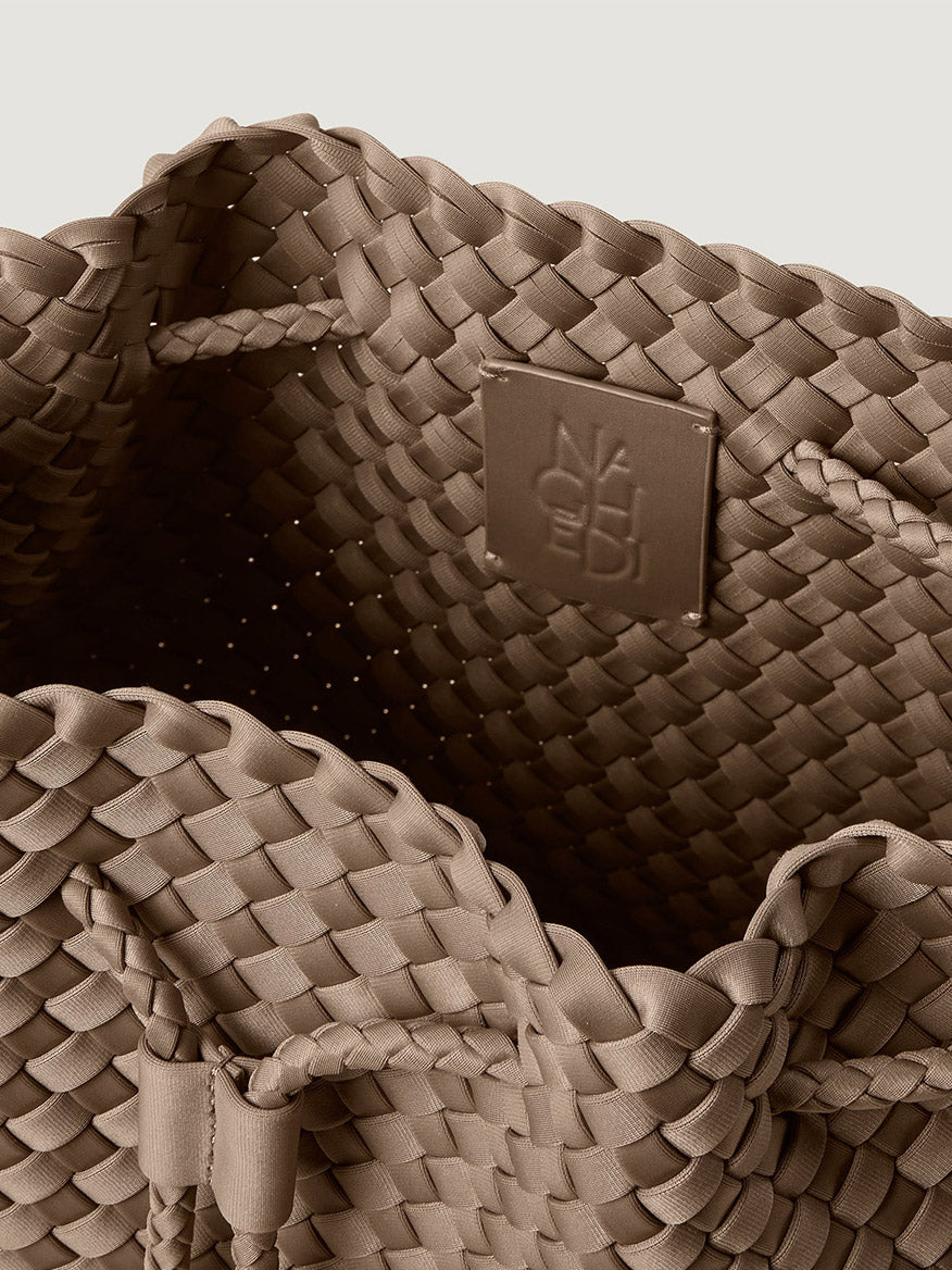 Close-up of the tan, handwoven interior of a Naghedi Mercer Large Bucket in Cashmere, featuring a brand logo patch.