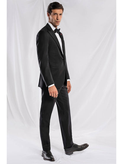 A man in a black Isaia Sanita AquaSpyder Peak Lapel Tuxedo with a bow tie, showcasing a classic fit with modern details, stands against a plain white background, looking directly at the camera.