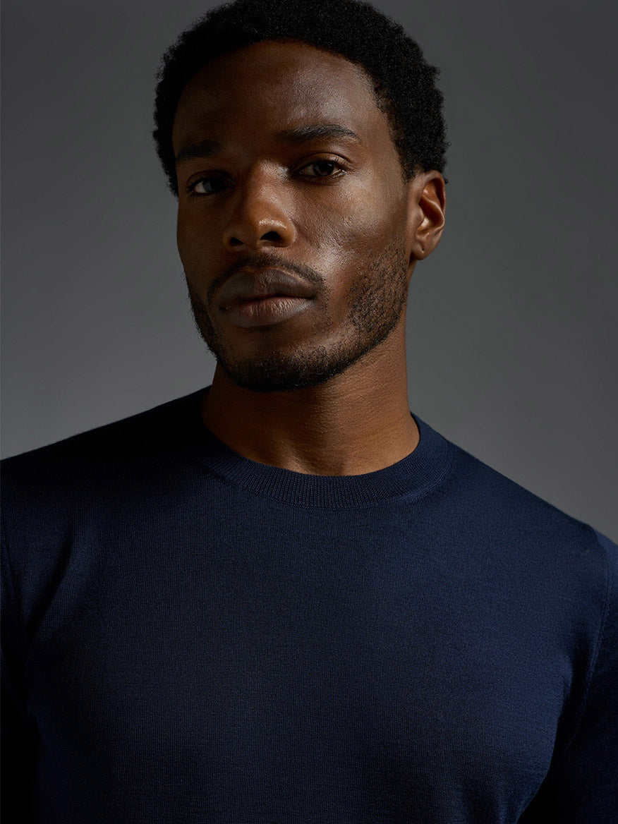 A man with short curly hair and a trimmed beard wears an Isaia Wool Cashmere Banded Tee in Navy, looking directly at the camera against a plain dark background.
