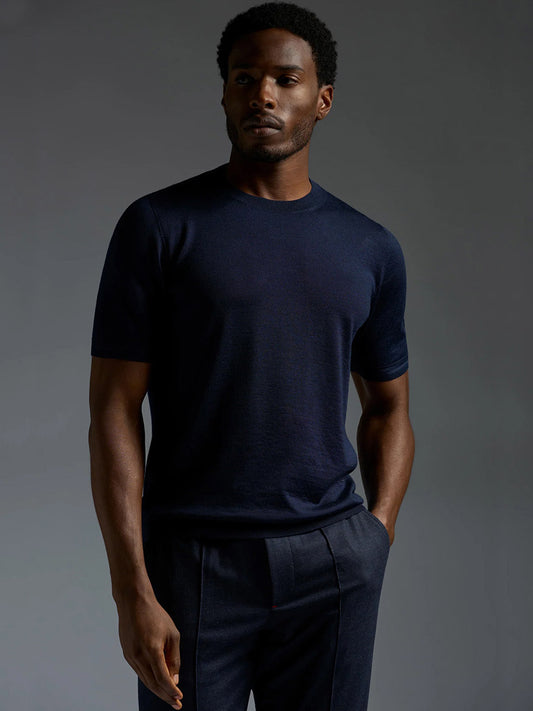 A man stands against a grey background wearing the Isaia Wool Cashmere Banded Tee in Navy and dark trousers, looking slightly to the side with a neutral expression.