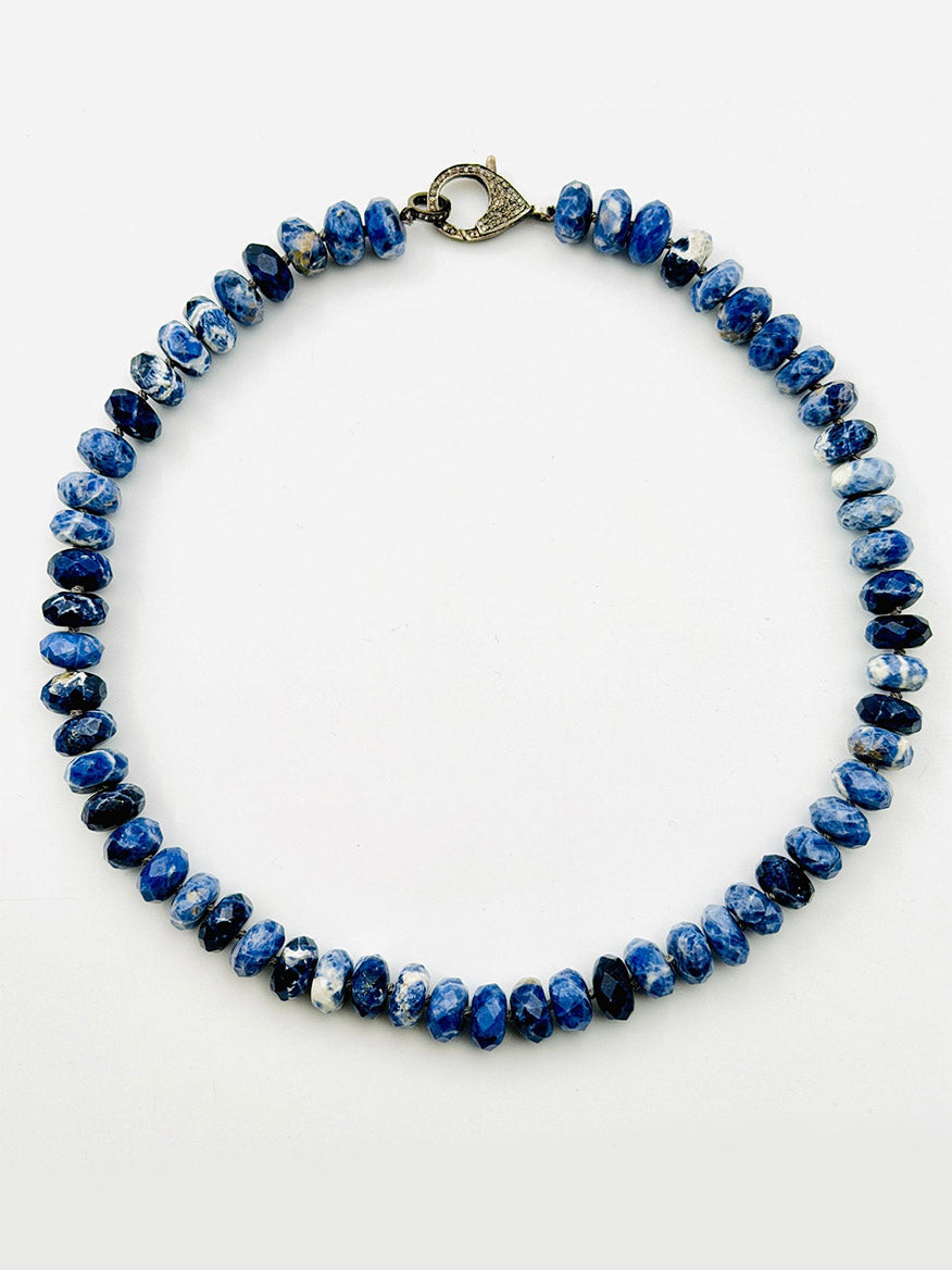 An 18-inch faceted sodalite rondelle necklace from JMNYC Designs, featuring blue and white stones and finished with a diamond clasp in sterling silver, arranged in a circular shape on a plain white background.