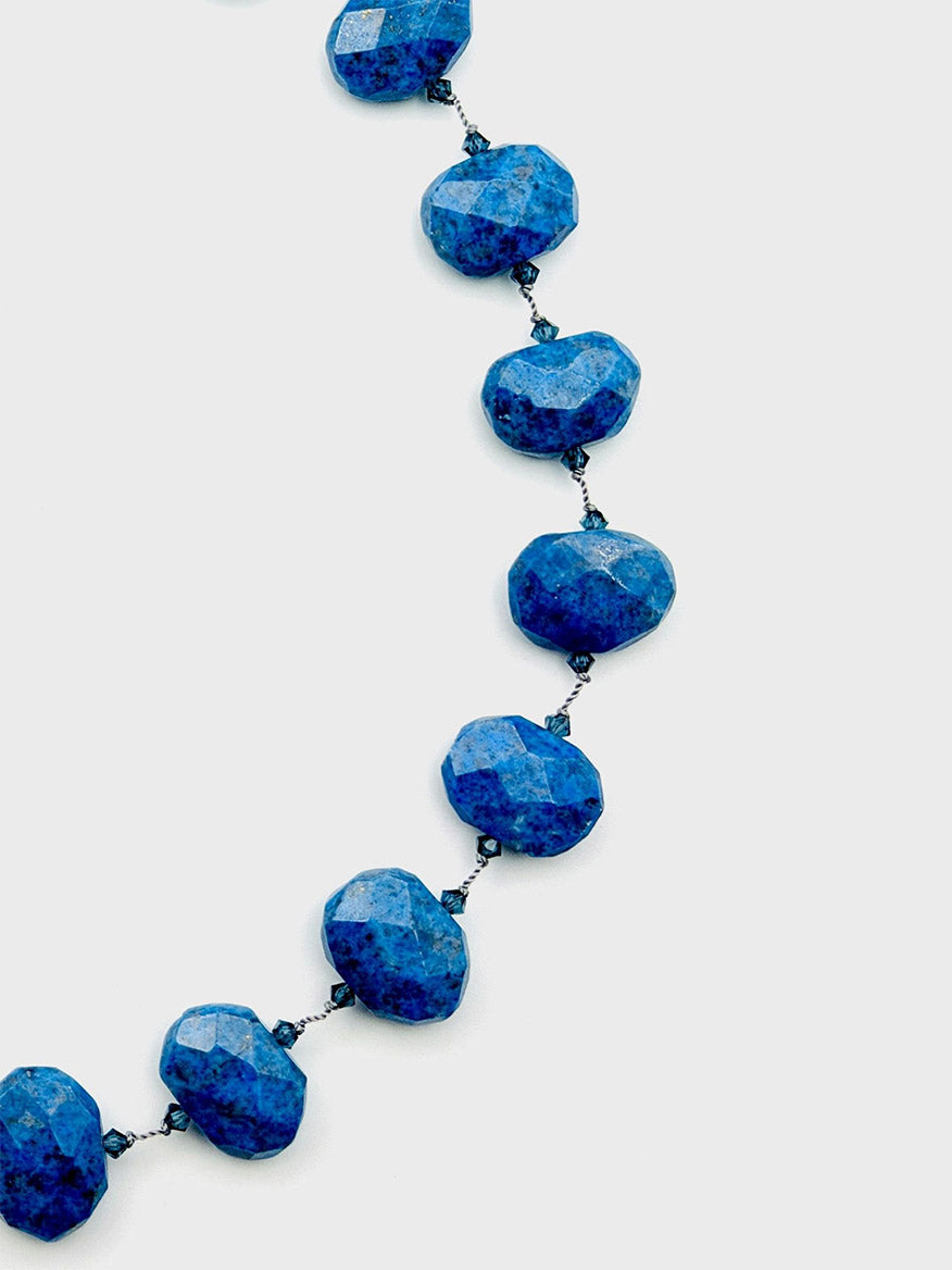 Close-up of the JMNYC Designs 18" Flat Faceted Denim Lapis Necklace, featuring large, denim lapis-inspired blue stones on a thin, dark metal chain against a plain white background. This elegant piece highlights the unique beauty of each thoughtfully cut gem.