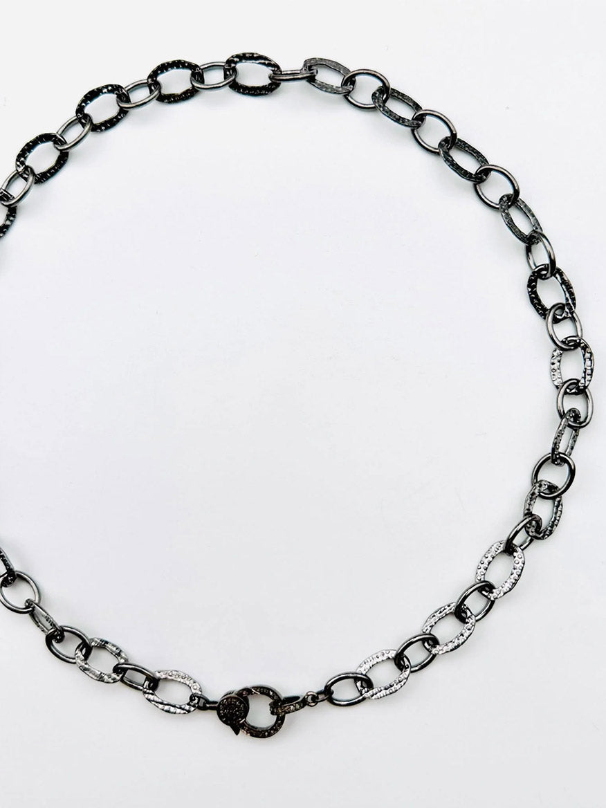 The JMNYC Designs 18" Hammered Oval Rhodium Plated Sterling Silver Chain features alternating silver and dark links arranged in a circle, finished with an elegant sterling silver diamond clasp at the bottom.