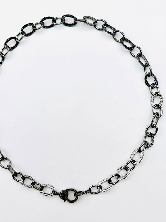The JMNYC Designs 18" Hammered Oval Rhodium Plated Sterling Silver Chain features alternating silver and dark links arranged in a circle, finished with an elegant sterling silver diamond clasp at the bottom.