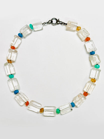 Introducing the JMNYC Designs 18" Crystal Quartz Cylinder Multi Stone Ball Necklace: a striking accessory featuring rectangular crystal quartz cylinder beads, interspersed with small, vibrant ball stones in turquoise, orange, blue, and yellow hues, and finished with a dark metal clasp.