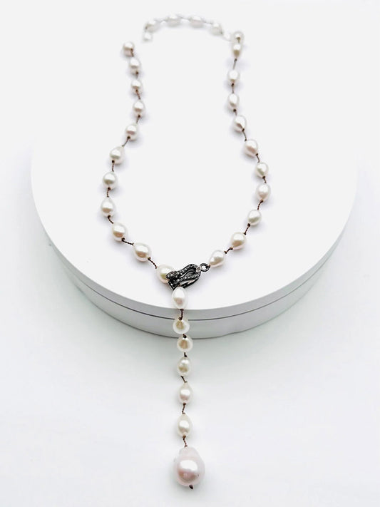 The JMNYC Designs 24" Small White Freshwater Baroque Pearl Lariat with Diamond Clasp features lustrous baroque pearls in a Y-shaped drop and is showcased on a white circular stand.