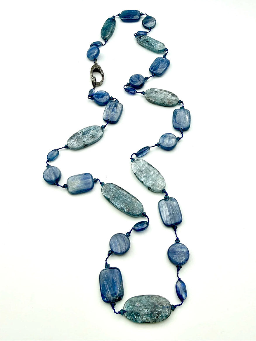 The JMNYC Designs 30" Multi Shape Blue Kyanite Necklace with Diamond Clasp showcases elegant, irregular blue kyanite beads in various shapes and sizes, each beautifully knotted on a dark cord and finished with a sparkling diamond clasp, all displayed against a white background.
