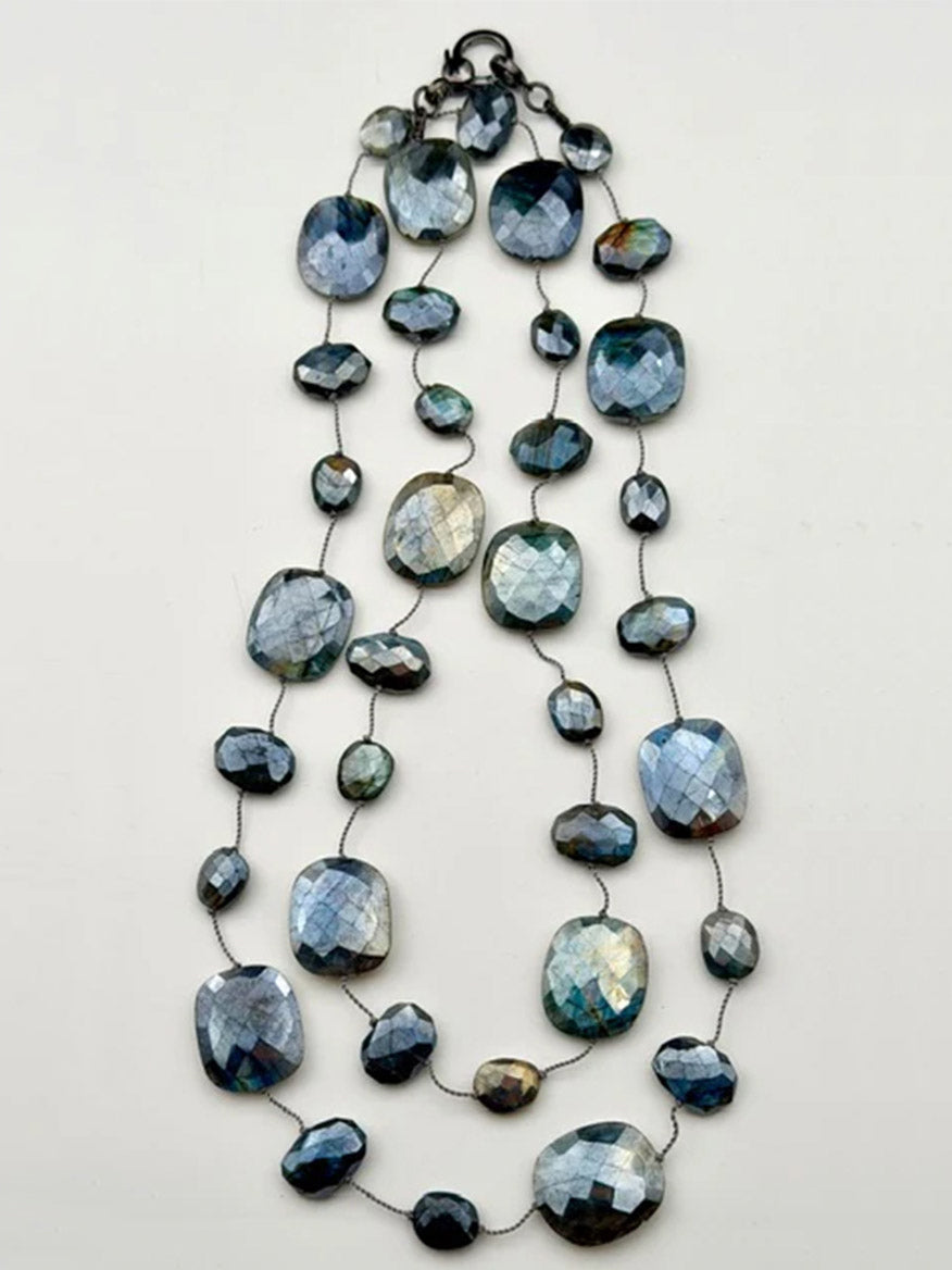The JMNYC Designs 36" Mystic Coated Labradorite Como Necklace showcases faceted oval and round, blue-gray iridescent labradorite gemstone beads linked by a thin wire, displayed on a plain background.