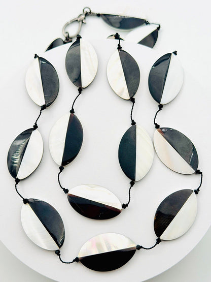 Introducing the JMNYC Designs 36" Oval Mother of Pearl and Black Tab Necklace—a bold statement piece showcasing oval beads split diagonally into black and mother of pearl halves. Each bead is artfully strung on a sleek black cord, creating a striking monochrome necklace.