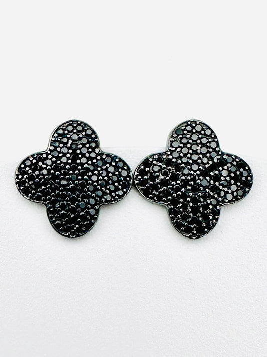 Introducing the JMNYC Designs Black Spinel Sterling Silver Clover Shaped Stud, 1.25"—a pair of striking black, four-leaf clover-shaped stud earrings carefully crafted in sterling silver. These earrings feature a textured, beaded surface accented with subtle Black Spinel stones and are beautifully displayed against a white background.