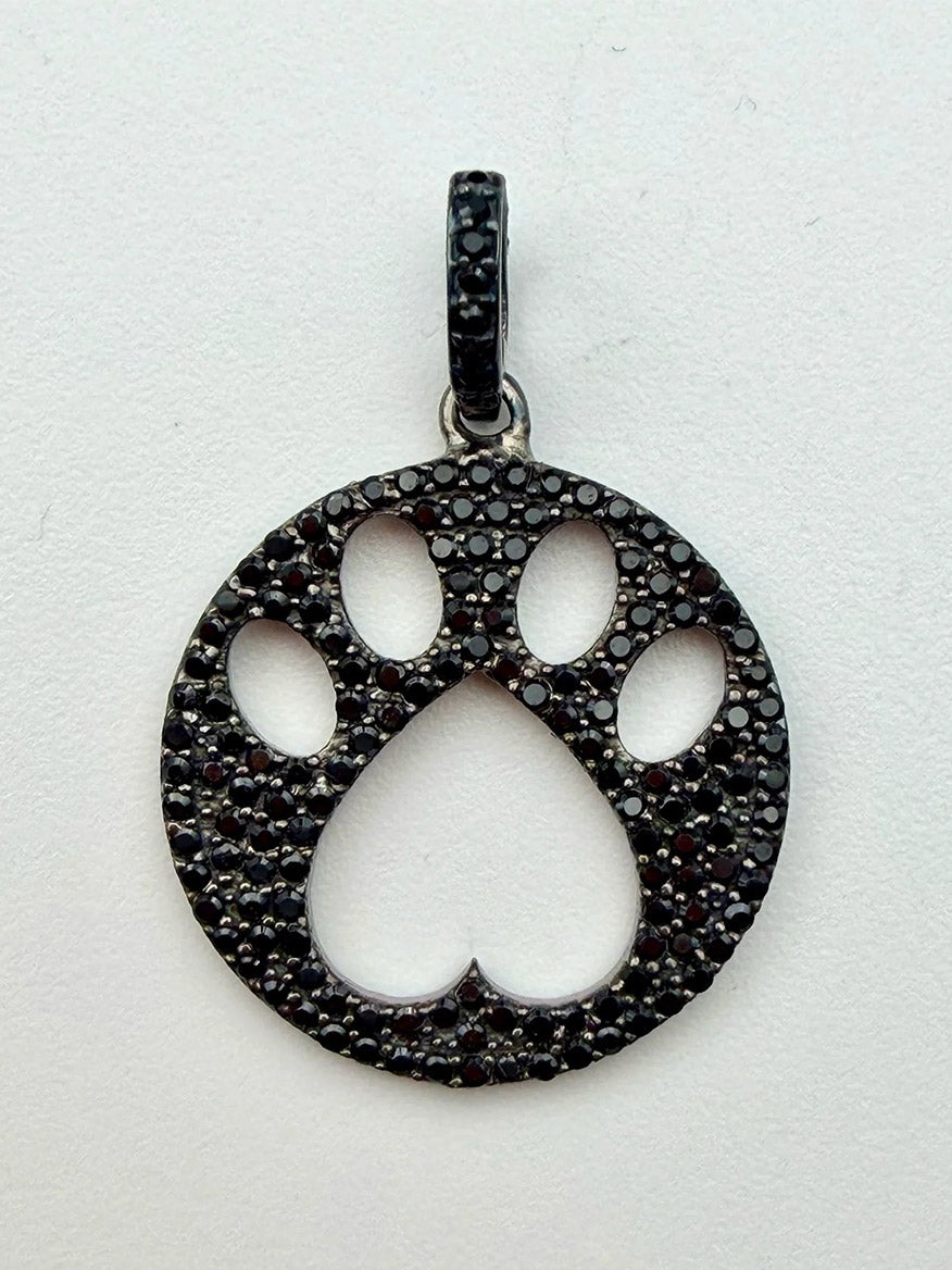 JMNYC Designs Black Spinel Dog Paw Sterling Silver Pendant showcases a round, cutout paw print design adorned with sparkling black spinel stones, displayed on a white background.