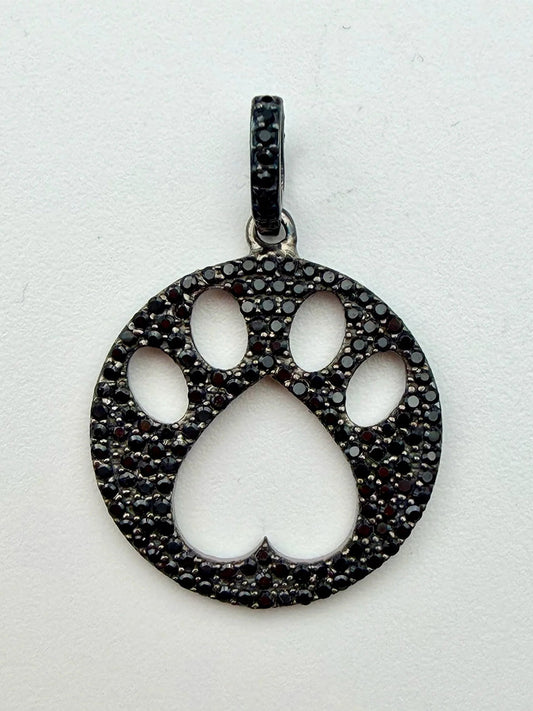 JMNYC Designs Black Spinel Dog Paw Sterling Silver Pendant showcases a round, cutout paw print design adorned with sparkling black spinel stones, displayed on a white background.