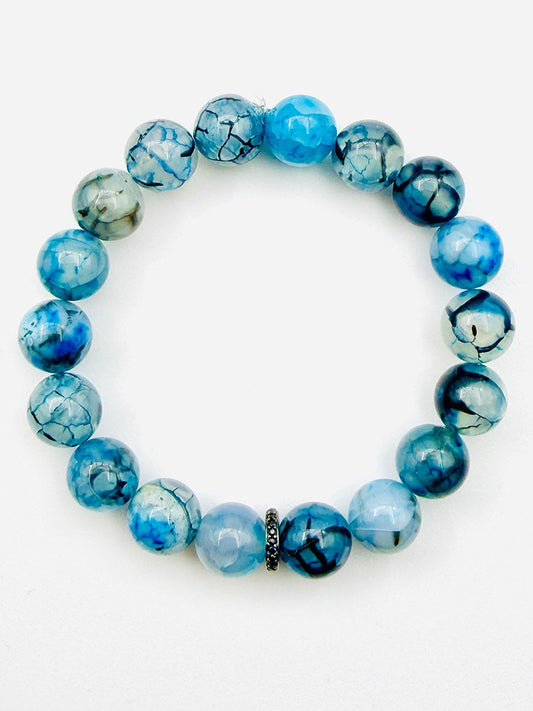 A limited edition 7.25" ball bracelet by JMNYC Designs, featuring striking Blue Impression Quartz marbled stones accented with a single textured Black Spinel rondelle, stands out beautifully against a white background.