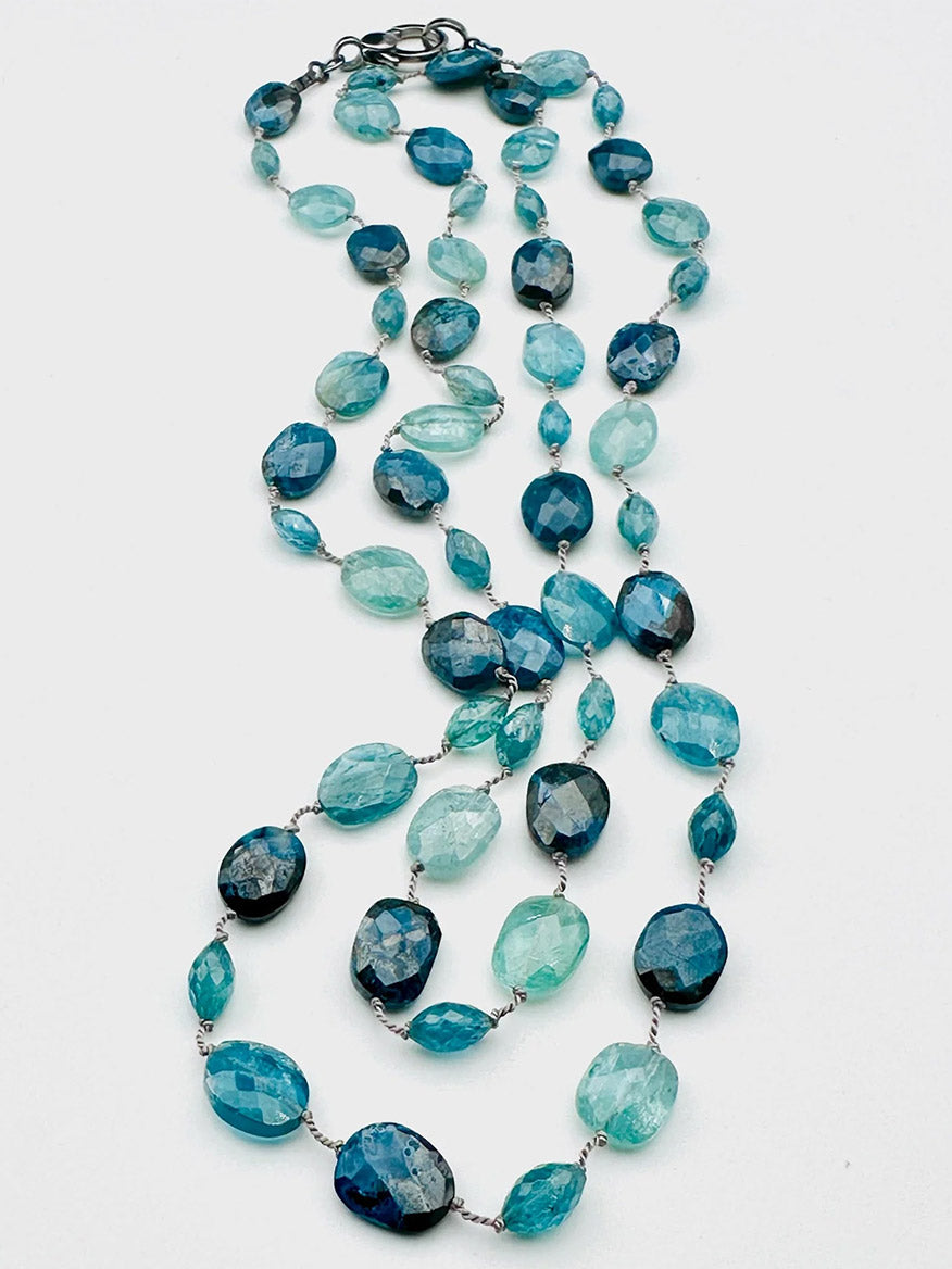 The JMNYC Designs Faceted Blue Kyanite & Chrysocolla Necklace, featuring blue, turquoise, and aqua beads in various shapes linked by small metal loops, is displayed on a white background.