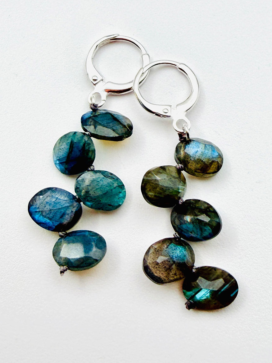 A pair of JMNYC Designs Faceted Oval Labradorite Earrings with Sterling Silver Huggie, each showcasing three vertically arranged oval labradorite stones, displayed against a white background.