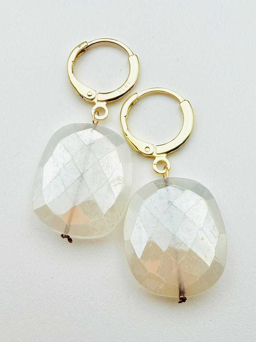 The JMNYC Designs Flat Faceted Mystic Rainbow Moonstone on Gold Filled Huggie, 1.25", features large, translucent moonstone pendants that catch the light beautifully, bringing a touch of subtle elegance to any look.