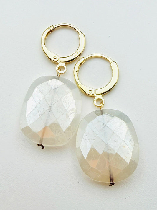 The JMNYC Designs Flat Faceted Mystic Rainbow Moonstone on Gold Filled Huggie, 1.25", features large, translucent moonstone pendants that catch the light beautifully, bringing a touch of subtle elegance to any look.