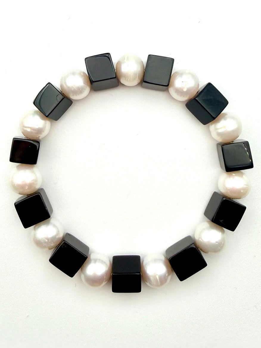 The JMNYC Designs Freshwater Pearl and Black Onyx Cube Stretch Bracelet, 7.35", showcases alternating white round freshwater pearls and black onyx cube beads, beautifully arranged in a circle on a white background.