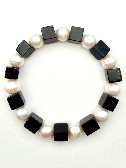 The JMNYC Designs Freshwater Pearl and Black Onyx Cube Stretch Bracelet, 7.35", showcases alternating white round freshwater pearls and black onyx cube beads, beautifully arranged in a circle on a white background.