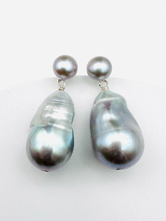 The JMNYC Designs Grey Freshwater Baroque Pearl Earrings showcase a pair of drop earrings featuring round and irregularly shaped silvery-gray freshwater pearls, elegantly displayed against a plain white background.